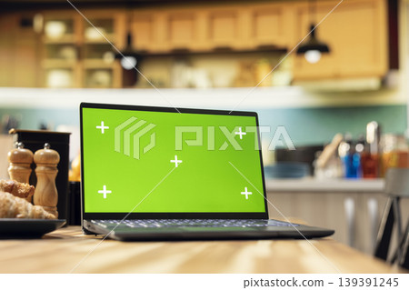 Green screen laptop on wooden table in empty bright kitchen, breakfast prepared with pastry, croissants and coffee. Warm tones on rustic furniture and kitchenware, cozy decorative items. Green screen laptop on wooden table in empty bright kitchen, breakfast prepared with pastry, croissants and coffee. Warm tones on rustic furniture and kitchenware, cozy decorative items. 139391245