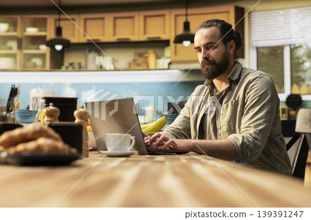 Remote worker, kitchen table with laptop, online work and tasks, professional lifestyle, connected male using technology, data tools for productivity. Teleworking from home, rustic interior. Remote worker, kitchen table with laptop, online work and tasks, professional lifestyle, connected male using technology, data tools for productivity. Teleworking from home, rustic interior. 139391247