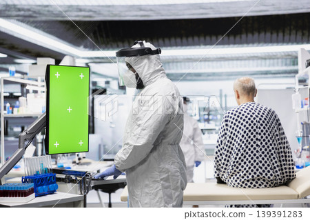 Vertical green screen next to male expert in coverall and mask observing contagious epidemic in lab, examining patient with serious symptoms. Preventing global disaster and health crisis. Vertical green screen next to male expert in coverall and mask observing contagious epidemic in lab, examining patient with serious symptoms. Preventing global disaster and health crisis. 139391283