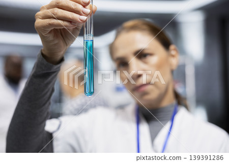 Woman medic checks DNA matter in a transparent test tube under laboratory light, analyzing chemical reaction and dosage data during a medical study for treatment improvement and discovery. Woman medic checks DNA matter in a transparent test tube under laboratory light, analyzing chemical reaction and dosage data during a medical study for treatment improvement and discovery. 139391286