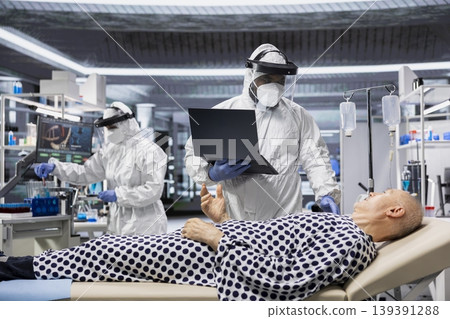 Medic in protective coveralls and gloves treats a patient in quarantine, analyzing infection data and testing vaccines to prevent outbreak spread and improve healthcare crisis. Medic in protective coveralls and gloves treats a patient in quarantine, analyzing infection data and testing vaccines to prevent outbreak spread and improve healthcare crisis. 139391288