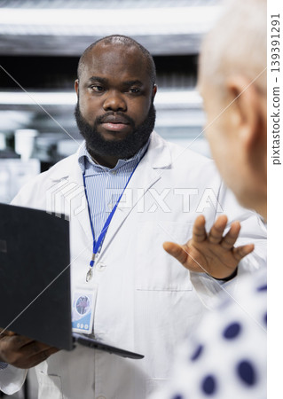 African american doctor explaining medical procedure during drug testing to old man, keeping senior patient under observation in research lab. Monitoring allergic reaction for progress. African american doctor explaining medical procedure during drug testing to old man, keeping senior patient under observation in research lab. Monitoring allergic reaction for progress. 139391291
