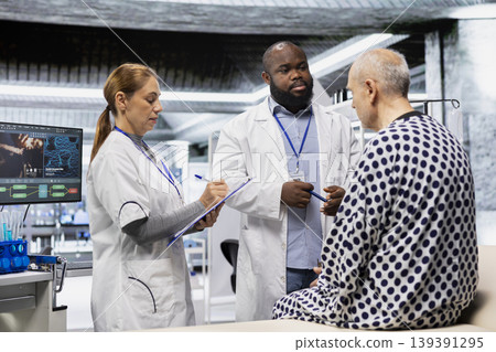 Two specialists conducting clinical trial in a research lab and monitoring patient during drug testing, recording dosage reactions and analyzing data to evaluate safety or risk for treatment. Two specialists conducting clinical trial in a research lab and monitoring patient during drug testing, recording dosage reactions and analyzing data to evaluate safety or risk for treatment. 139391295
