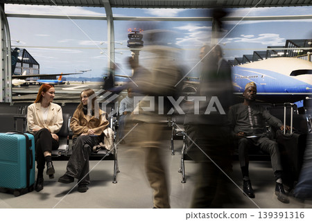 Smiling women talking in busy airport surrounded by multiethnic rushing blurry travelers. Sisters sitting on chairs waiting for plane and silhouette of people hurrying to fly home during holidays Smiling women talking in busy airport surrounded by multiethnic rushing blurry travelers. Sisters sitting on chairs waiting for plane and silhouette of people hurrying to fly home during holidays 139391316