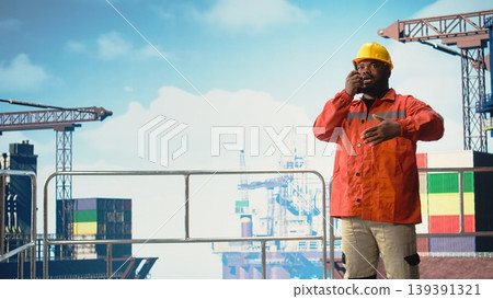 Expert inspects integrity of offshore platform infrastructure, speaking in walkie talkie. African american man on drilling rig using handheld radio device to communicate malfunctions, Expert inspects integrity of offshore platform infrastructure, speaking in walkie talkie. African american man on drilling rig using handheld radio device to communicate malfunctions, 139391321