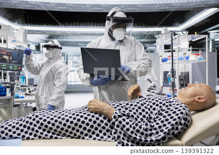 Doctor in biohazard lab conducts medical trial on a contagious patient, studying disease transmission, symptoms and antiviral drug effectiveness to develop treatments in virology. Doctor in biohazard lab conducts medical trial on a contagious patient, studying disease transmission, symptoms and antiviral drug effectiveness to develop treatments in virology. 139391322