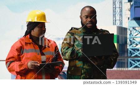Military personnel stationed on offshore rig evaluating surveillance footage. Soldier provides protection to drilling barge and engineer controlling remote systems with devices Military personnel stationed on offshore rig evaluating surveillance footage. Soldier provides protection to drilling barge and engineer controlling remote systems with devices 139391349