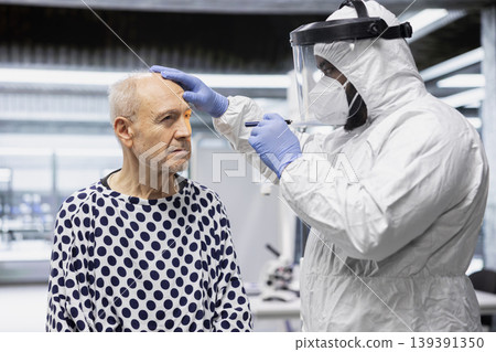 Black specialist dressed in hazmat suit monitoring patient for symptoms of contagious disease during epidemic response, conducting laboratory research on vaccines. Antiviral therapy. 139391350