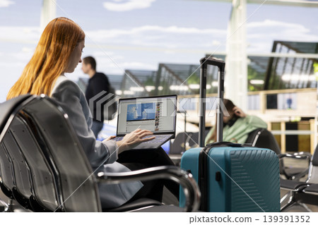 Woman traveler viewing online videos on streaming platform in the airport, with boarding pass and luggage nearby. Modern lifestyle habits and everyday experience of fun social media content. Woman traveler viewing online videos on streaming platform in the airport, with boarding pass and luggage nearby. Modern lifestyle habits and everyday experience of fun social media content. 139391352