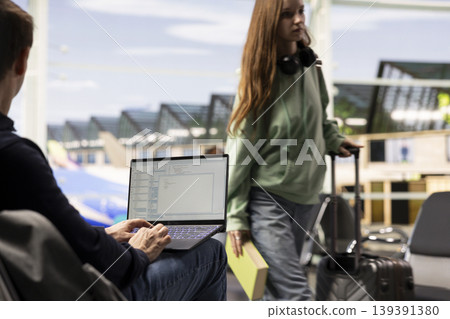 Man digital nomad, focused on programming, system development on laptop, in the airport terminal, surrounded by passengers. Coding and data processing via flexible job mobility. Man digital nomad, focused on programming, system development on laptop, in the airport terminal, surrounded by passengers. Coding and data processing via flexible job mobility. 139391380
