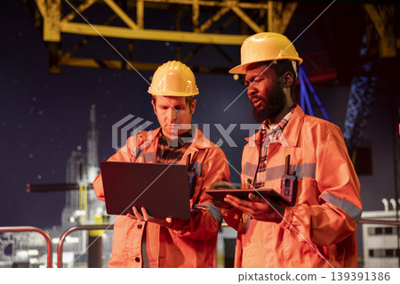 Industrial engineers inspect offshore drilling rig systems using gadgets to monitor emissions while extracting natural gas and petroleum. Ensuring efficient oil production for the industry. 139391386