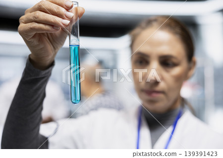 Close up of female expert checking element from test tube in a modern lab, recording chemical reaction and data for a new product development. Research trial drug testing for innovation. Close up of female expert checking element from test tube in a modern lab, recording chemical reaction and data for a new product development. Research trial drug testing for innovation. 139391423