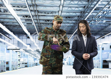 Military man talks with manager about using silicon wafer supply chain for national security purposes. Army officer and management executive reviewing strategic microelectronics factory production Military man talks with manager about using silicon wafer supply chain for national security purposes. Army officer and management executive reviewing strategic microelectronics factory production 139391474