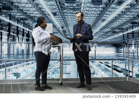 Female director and microchip smart factory colleague analyze silicon wafer production lines bottlenecks. Employees looking at data on screen, improving semiconductor substrates supply chain yield Female director and microchip smart factory colleague analyze silicon wafer production lines bottlenecks. Employees looking at data on screen, improving semiconductor substrates supply chain yield 139391489