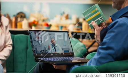 Elderly man attending e-health consultation via video call with doctor, showing box of supplements and ensuring correct dosage or administration. Medical professional offers advice on medicine. Elderly man attending e-health consultation via video call with doctor, showing box of supplements and ensuring correct dosage or administration. Medical professional offers advice on medicine. 139391530