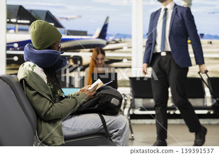 Busy airport departure area with female traveler checking flight schedule, looking at screen and reviewing boarding pass information. Waiting area with passengers preparing for flying. Busy airport departure area with female traveler checking flight schedule, looking at screen and reviewing boarding pass information. Waiting area with passengers preparing for flying. 139391537
