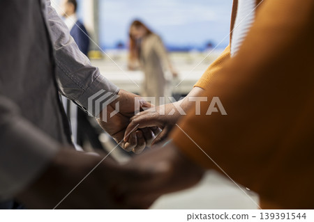 Close up of partners holding hands in crowded airport lounge area, symbolizing devotion and connection before overseas journey. Authentic romantic moment before honeymoon travel. Close up of partners holding hands in crowded airport lounge area, symbolizing devotion and connection before overseas journey. Authentic romantic moment before honeymoon travel. 139391544