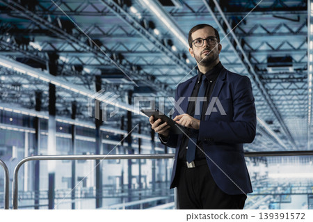 Man checking infrastructure malfunctions in industry 4.0 manufacturing plant with tablet. Management executive assessing modern smart factory semiconductor yields using device Man checking infrastructure malfunctions in industry 4.0 manufacturing plant with tablet. Management executive assessing modern smart factory semiconductor yields using device 139391572