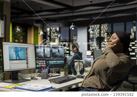 Woman film editor yawning and stretching her back on chair at night, feeling overburdened and weary to finish video editing project in time. Videographer working under pressure, fatigued. Woman film editor yawning and stretching her back on chair at night, feeling overburdened and weary to finish video editing project in time. Videographer working under pressure, fatigued. 139391582