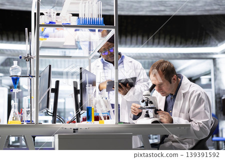 Team of experts investigate molecular samples at microscope with laboratory tray and lens system, magnification tools support diagnostics and biotechnology breakthrough in healthcare science. Team of experts investigate molecular samples at microscope with laboratory tray and lens system, magnification tools support diagnostics and biotechnology breakthrough in healthcare science. 139391592