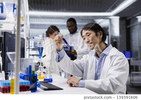 Senior chemical engineer investigates chemical sample properties using test tube in sterile laboratory setting. Asian research lab specialist holds vial containing new compound, doing scientific RD Senior chemical engineer investigates chemical sample properties using test tube in sterile laboratory setting. Asian research lab specialist holds vial containing new compound, doing scientific RD 139391606