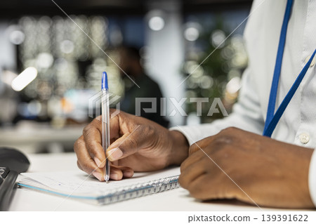 Close up of black businessman transcribing key points on notebook after hours. Employee creating a summary, proofreading numbers and designing strategy to align with company targets. 139391622