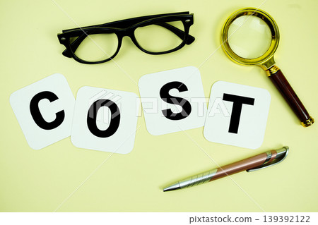 COST alphabet letters with magnifying glass, eye glasses and pen on yellow background 139392122
