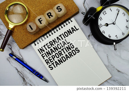 IFRS International Financial Reporting Standards text written on notepad with magnifying glass and alarm clock on marble background 139392211