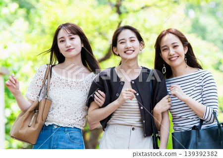 一群女孩在綠樹環繞的公園散步;她們是閨蜜,正在進行一次旅行。 一群女孩在綠樹環繞的公園散步;她們是閨蜜,正在進行一次旅行。 139392382