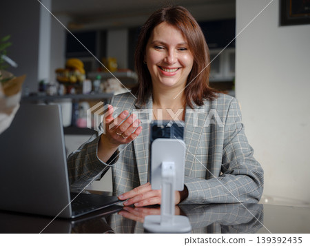 Mother working remotely from home, multitasking between professional tasks and family responsibilities, using a laptop in a cozy home environment. Mother working remotely from home, multitasking between professional tasks and family responsibilities, using a laptop in a cozy home environment. 139392435