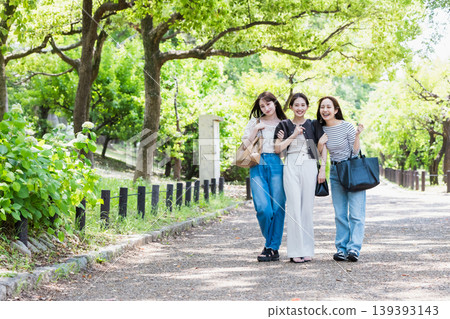 一群女孩在綠樹環繞的公園散步;她們是閨蜜,正在進行一次旅行。 一群女孩在綠樹環繞的公園散步;她們是閨蜜,正在進行一次旅行。 139393143