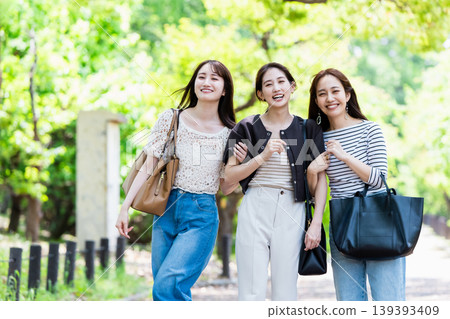 一群女孩在綠樹環繞的公園散步;她們是閨蜜,正在進行一次旅行。 一群女孩在綠樹環繞的公園散步;她們是閨蜜,正在進行一次旅行。 139393409