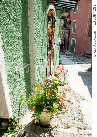 A building with pastel-colored walls and flowers in potted plants under bright sunlight on the French island of Corsica in the Mediterranean Sea. A building with pastel-colored walls and flowers in potted plants under bright sunlight on the French island of Corsica in the Mediterranean Sea. 139394288