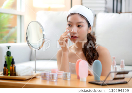 Beautiful young asian woman smile with skin care use oil blotting paper on face looking mirror. 139394309
