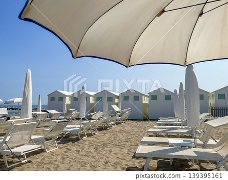 Beach Lounge Chairs and Umbrellas with Coastal Cabins in Lido di Venezia, Italy. Beach Lounge Chairs and Umbrellas with Coastal Cabins in Lido di Venezia, Italy. 139395161