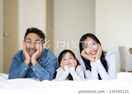 A Japanese mother and child resting their chin on their hands while lying on a hotel bed. A Japanese mother and child resting their chin on their hands while lying on a hotel bed. 139395235