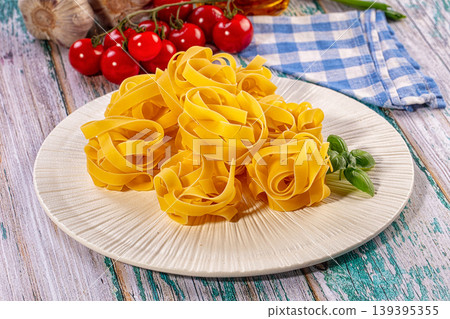 Fresh uncooked tagliatelle pasta nests on plate with cherry tomatoes, garlic, basil, rustic wooden background Fresh uncooked tagliatelle pasta nests on plate with cherry tomatoes, garlic, basil, rustic wooden background 139395355
