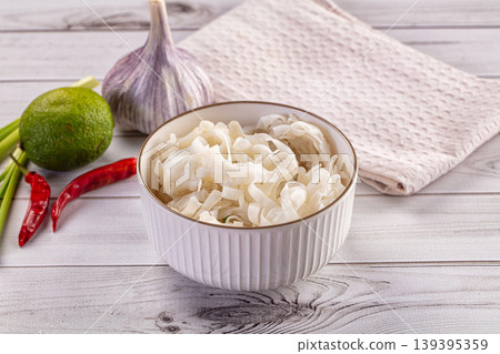 Bowl of rice noodles with fresh garlic, lime, and chili peppers on a white wooden table. 139395359