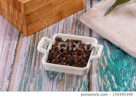 Dried whole cloves spice in a white bowl on a rustic painted wood surface with a bamboo box and linen napkin Dried whole cloves spice in a white bowl on a rustic painted wood surface with a bamboo box and linen napkin 139395399