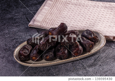 Pile of dark brown Medjool dates on oval plate. Healthy fruit snack on textured background Pile of dark brown Medjool dates on oval plate. Healthy fruit snack on textured background 139395430