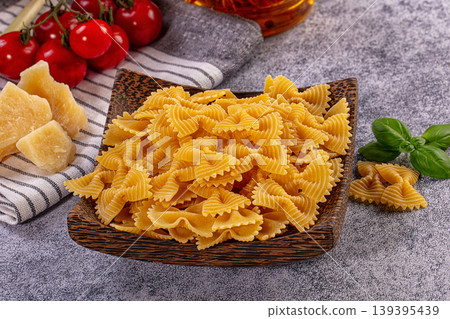 Raw farfalle bow tie pasta in rustic wooden bowl, surrounded by fresh cherry tomatoes, parmesan cheese chunks, green onions, basil. Bright, inviting composition Raw farfalle bow tie pasta in rustic wooden bowl, surrounded by fresh cherry tomatoes, parmesan cheese chunks, green onions, basil. Bright, inviting composition 139395439