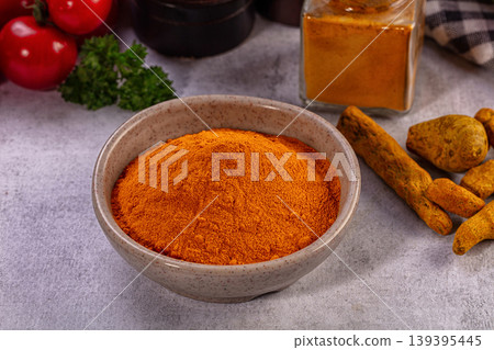 Bright orange turmeric powder in ceramic bowl, fresh red tomatoes, green parsley, whole roots, spice jar on grey surface Bright orange turmeric powder in ceramic bowl, fresh red tomatoes, green parsley, whole roots, spice jar on grey surface 139395445