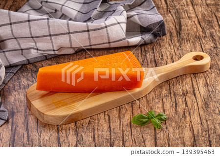 Orange cheese wedge on wooden cutting board, rustic background, fresh basil leaves 139395463