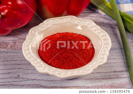 Red paprika powder in white ceramic bowl with bell peppers and green onions on rustic wooden table Red paprika powder in white ceramic bowl with bell peppers and green onions on rustic wooden table 139395479