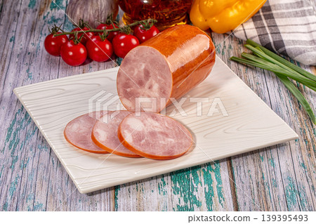 Sliced boiled ham sausage on white plate with fresh vegetables on rustic wooden table 139395493
