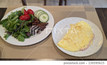 A plate of ham and cheese omelette and a salad plate of olives, cucumbers and tomatoes 139395615