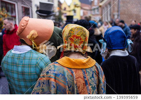 Deventer, Overijssel, Netherlands - 14.12.2025: Rear view of women wearing colorful Victorian bonnets and patterned capes at a historical festival. A festive scene on a crowded European city street. Deventer, Overijssel, Netherlands - 14.12.2025: Rear view of women wearing colorful Victorian bonnets and patterned capes at a historical festival. A festive scene on a crowded European city street. 139395659