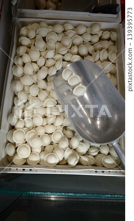 White dumpling wrappers piled in a container with a metal scoop resting on top, showcasing the texture and shape of the uncooked dough pieces White dumpling wrappers piled in a container with a metal scoop resting on top, showcasing the texture and shape of the uncooked dough pieces 139395773