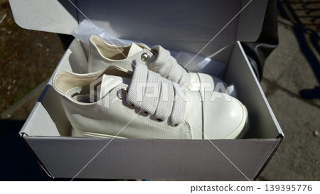 White sneakers with elastic laces displayed in an open shoe box on a textured surface, sunlight illuminating the scene and highlighting the shoe details White sneakers with elastic laces displayed in an open shoe box on a textured surface, sunlight illuminating the scene and highlighting the shoe details 139395776