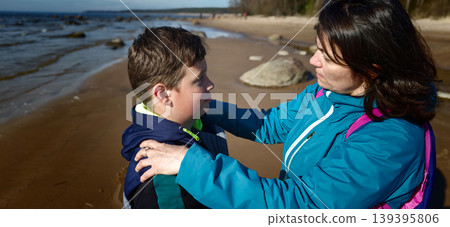 Mother and son engaged in a serious conversation on a sandy beach, with the ocean and distant trees visible in the background Mother and son engaged in a serious conversation on a sandy beach, with the ocean and distant trees visible in the background 139395806